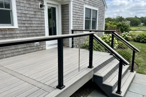 Close-up of a modern gray composite deck with black posts, cable railings, and stairs with a matching handrail.