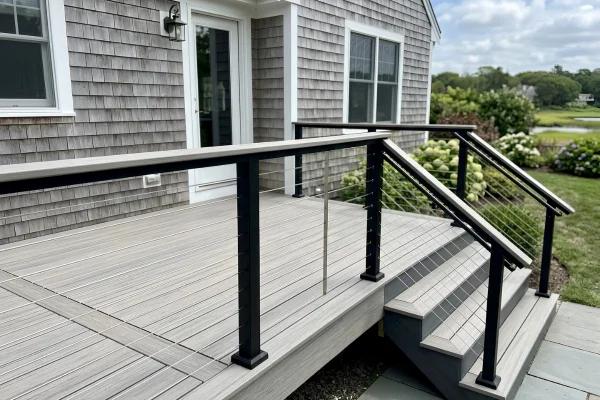 Close-up of a modern gray composite deck with black posts, cable railings, and stairs with a matching handrail.